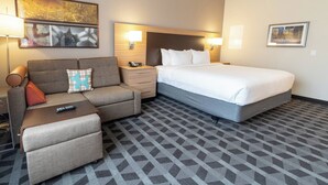 Une chambre d’hôtel avec un lit, un canapé, une petite table, une table de chevet et une lampe.