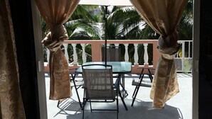 Un balcone con tavolo e sedie, tende e vista su palme.