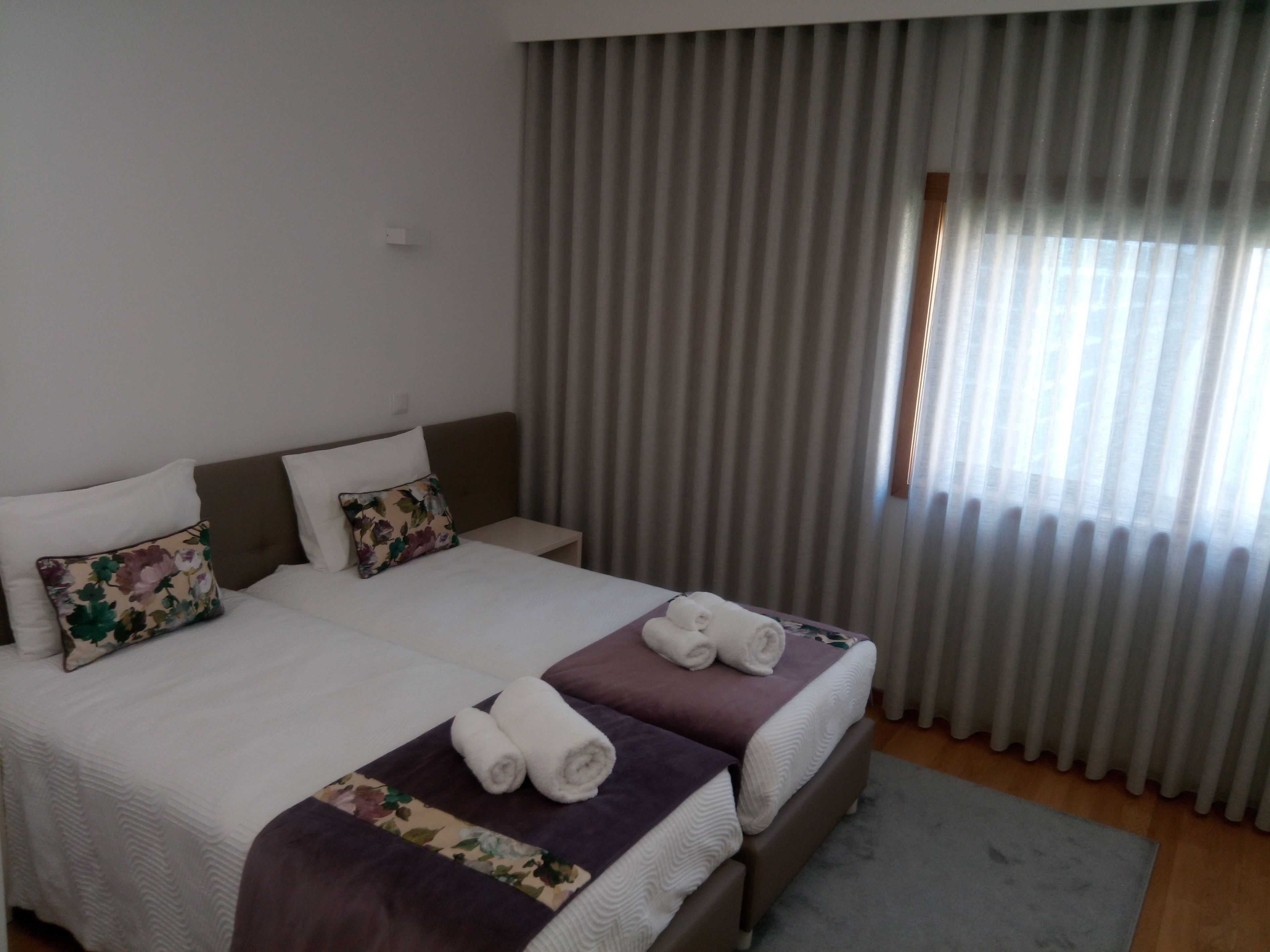 A double bed with two pillows, a nightstand, and a window with curtains.