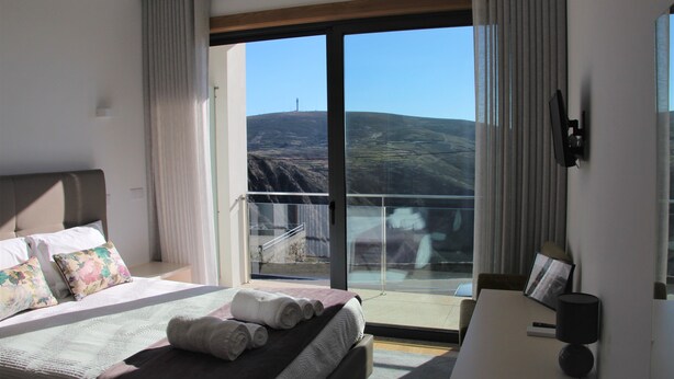 A hotel room with a large bed, a desk, and a balcony with a view of the landscape. - Hotel Rural da Freita (Arouca)