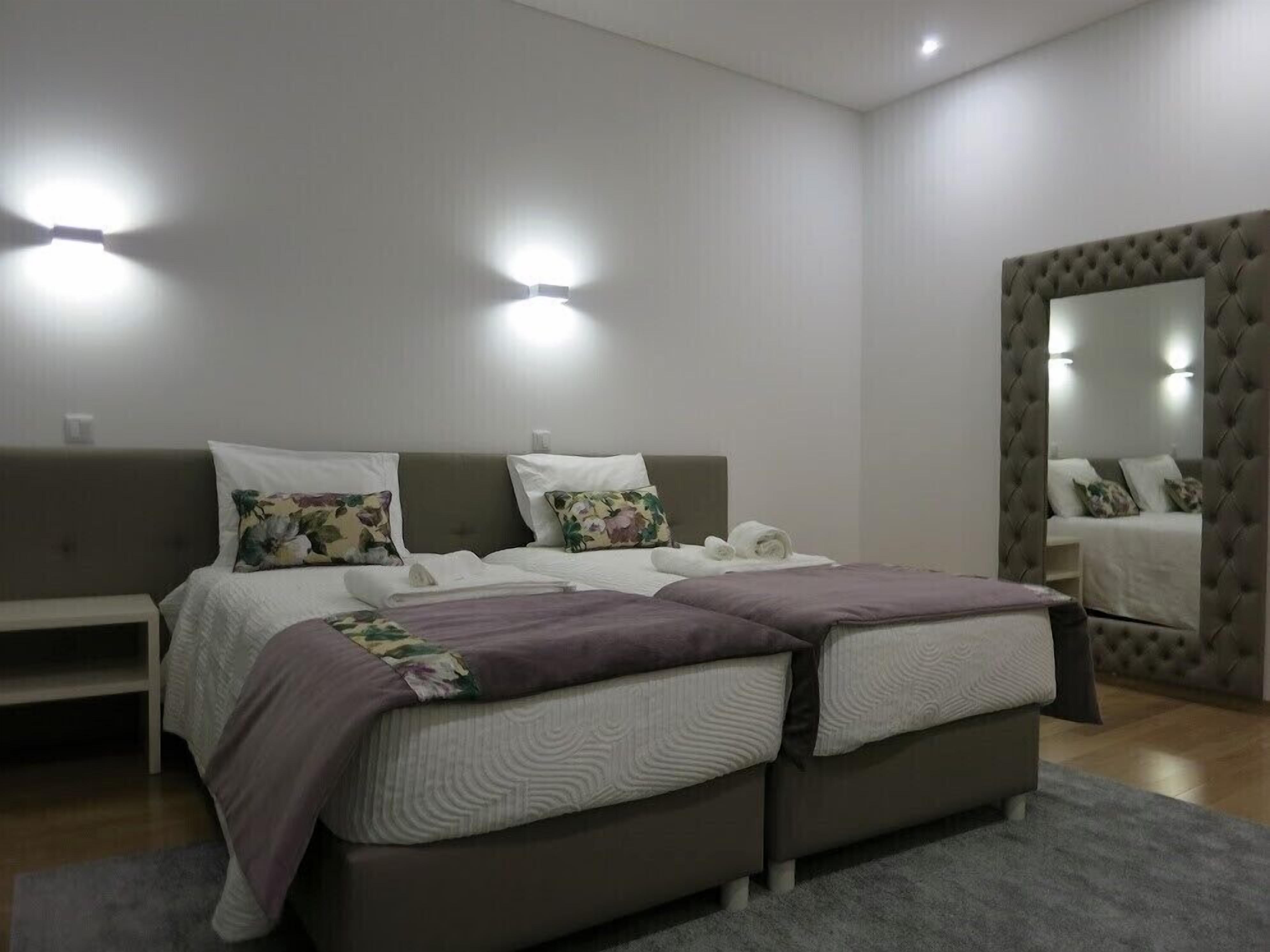 A modern bedroom with two beds, a large mirror, and built-in lighting.