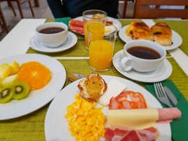 Desayuno con platos de huevos, fruta y bollería, además de tazas de café y zumo de naranja.
