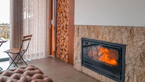 A modern living room with a fireplace, a stone wall, and a wooden bench. - Hotel Rural da Freita (Arouca)