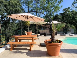 A poolside area with outdoor furniture, including a table and chairs, surrounded by large umbrellas.