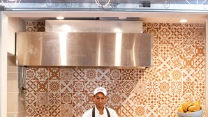Un chef en la barra, con diversos alimentos y una campana extractora de acero inoxidable grande sobre ella.
