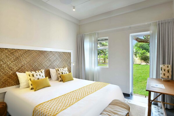 Habitación de hotel con una cama grande, cabecera de madera y vista a un jardín a través de una puerta corrediza de vidrio.