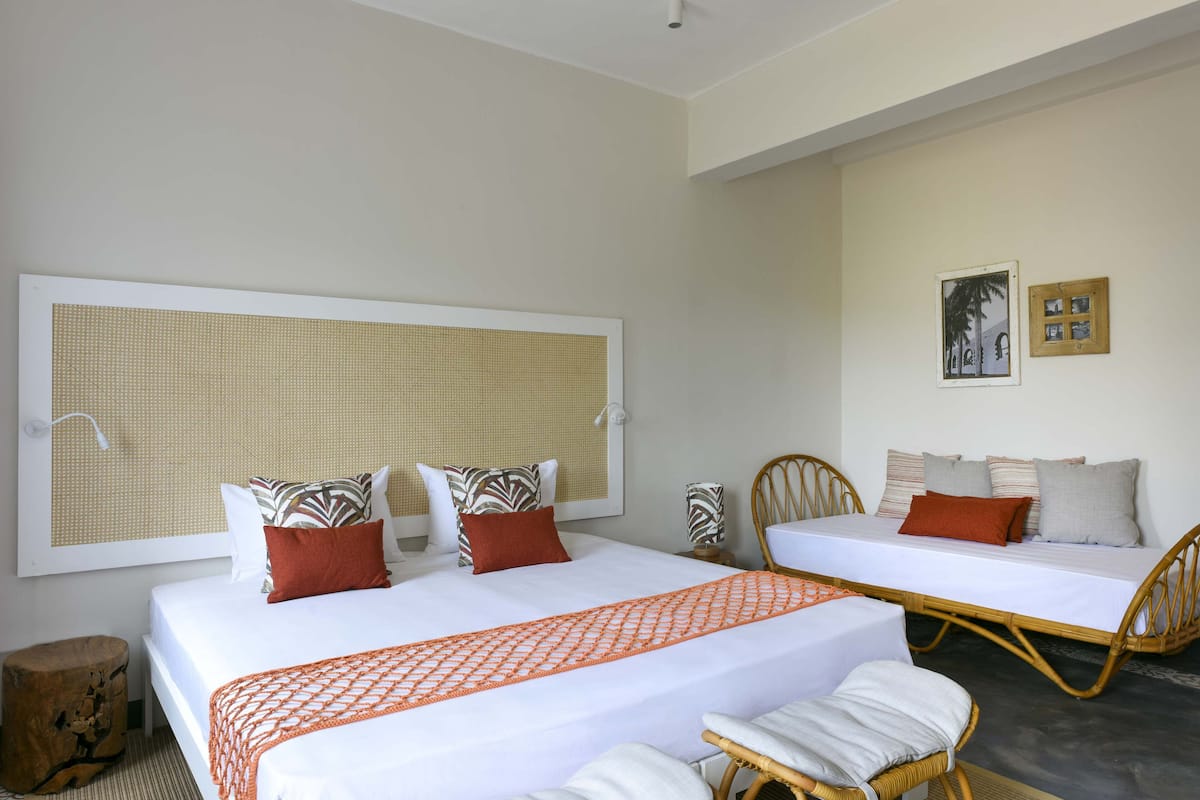 A hotel room with two beds, a large window with a woven blind, and a framed picture on the wall.