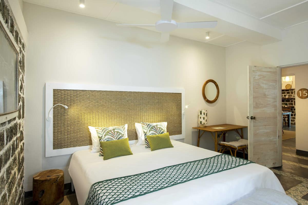 A hotel room with a large bed, a desk, and a view of a stone wall.