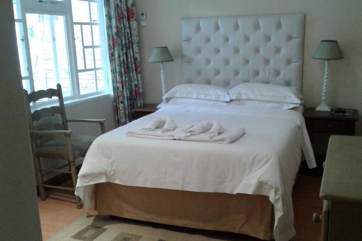 Una cama bien hecha con sábanas y toallas blancas, un cabecero capitonado, dos lámparas de noche y una mesita con una lámpara.