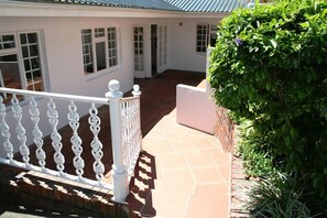 Un edificio blanco con un patio empedrado, barandillas blancas y un arbusto verde.