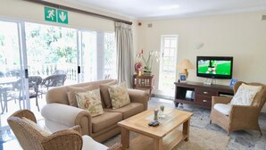 A living room with a sofa, two armchairs, a coffee table, a television, and a view of the outdoors through large windows. - The WhiteHouse B&B (Westville)