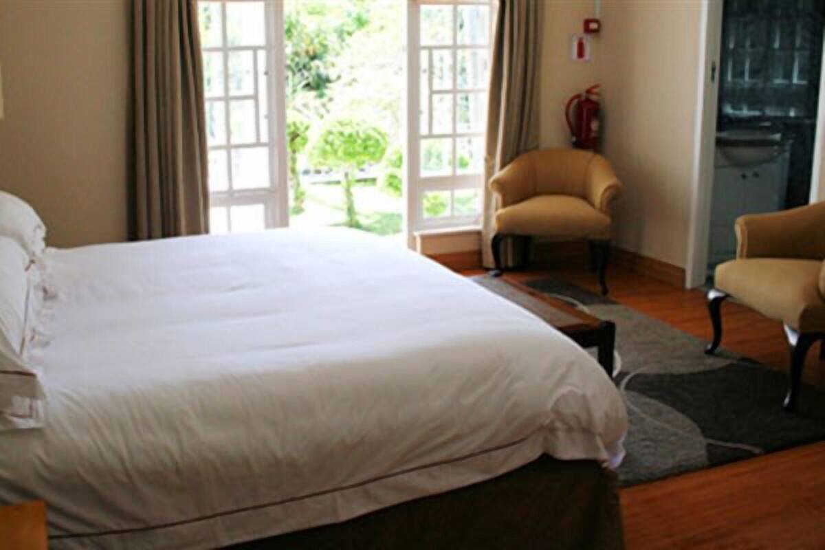 Habitación de hotel con una cama grande, dos sillones y vistas a zonas verdes a través de las ventanas.