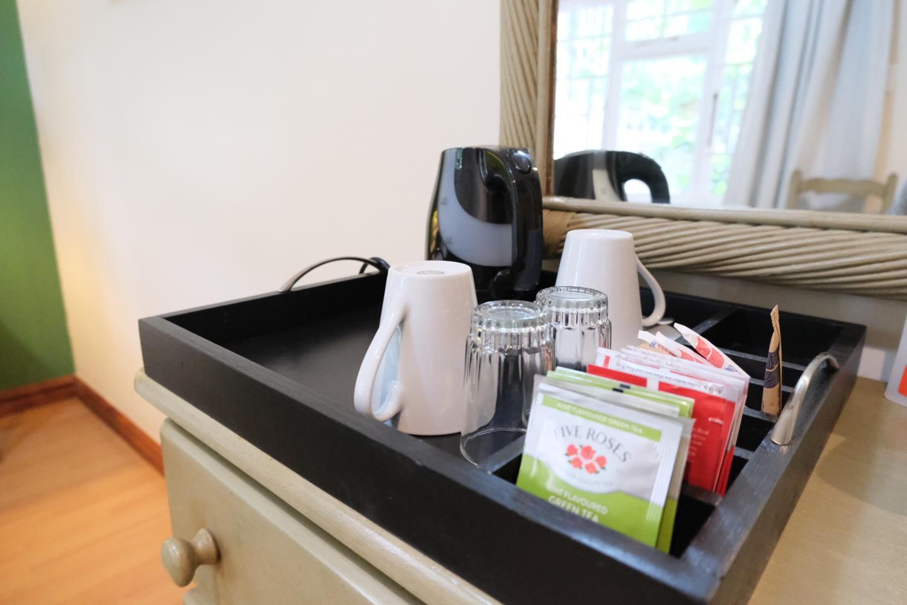 A hotel room with a black tray table holding a white mug, a glass, a pack of tea, and a black device.
