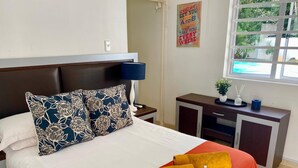 A neatly made bed with a floral pillow, a red bedspread, and two yellow towels. There is a nightstand with a lamp and a small cabinet with a plant on top. - The WhiteHouse B&B (Westville)