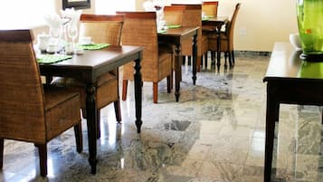 A dining area with marble flooring, wooden dining tables and chairs, and a green vase on one table.