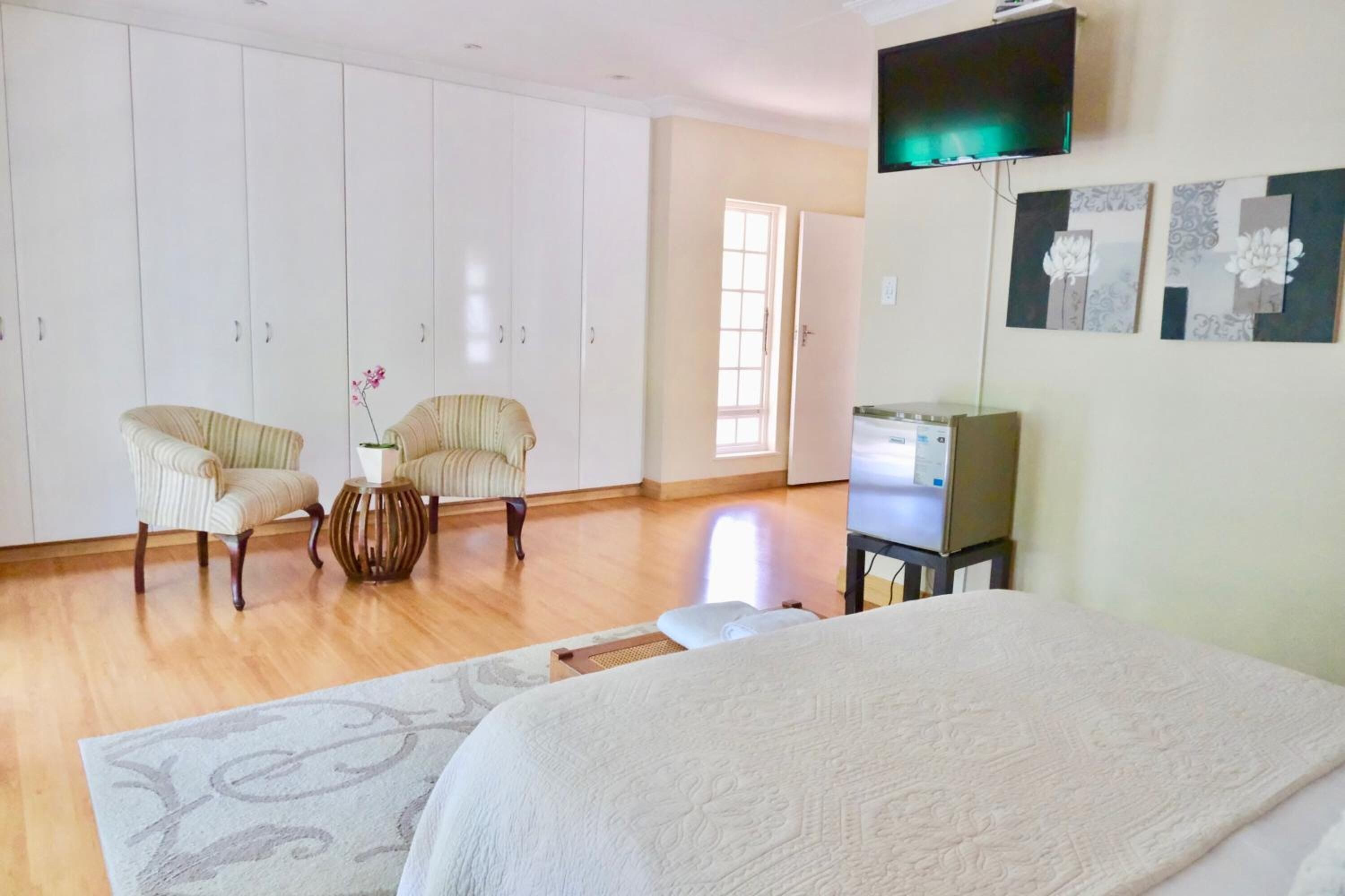 A bedroom with a bed, two chairs, a small table with a vase, a television, and a wardrobe.