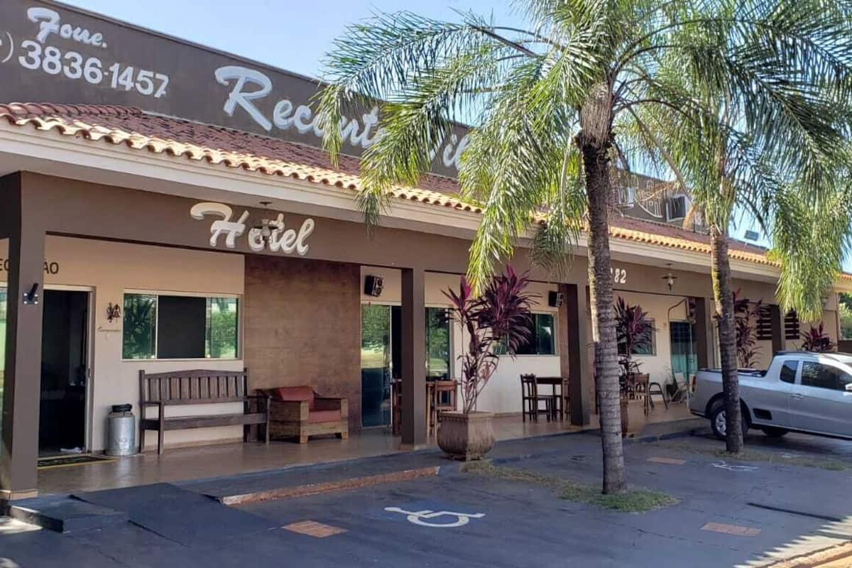 A hotel with a signboard, outdoor seating, and a parked car.