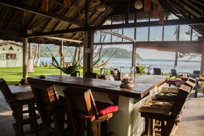 Un bar situé en bord de mer, avec des meubles en bois, un hamac et une vue sur l’océan.