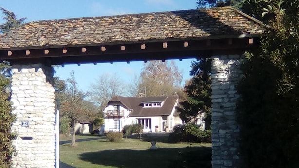 A stone archway leading to a house with a stone facade and a tiled roof.