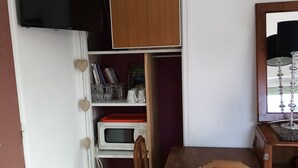 A compact room with a wooden table and chairs, a television mounted on the wall, and a built-in bookshelf with various items.