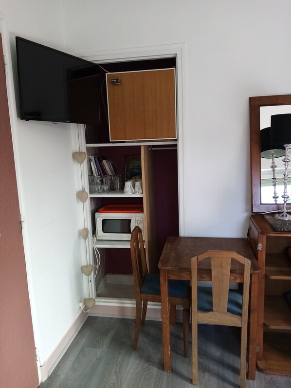 Una habitación compacta con una mesa y sillas de madera, un televisor en la pared y una estantería empotrada con varios objetos.