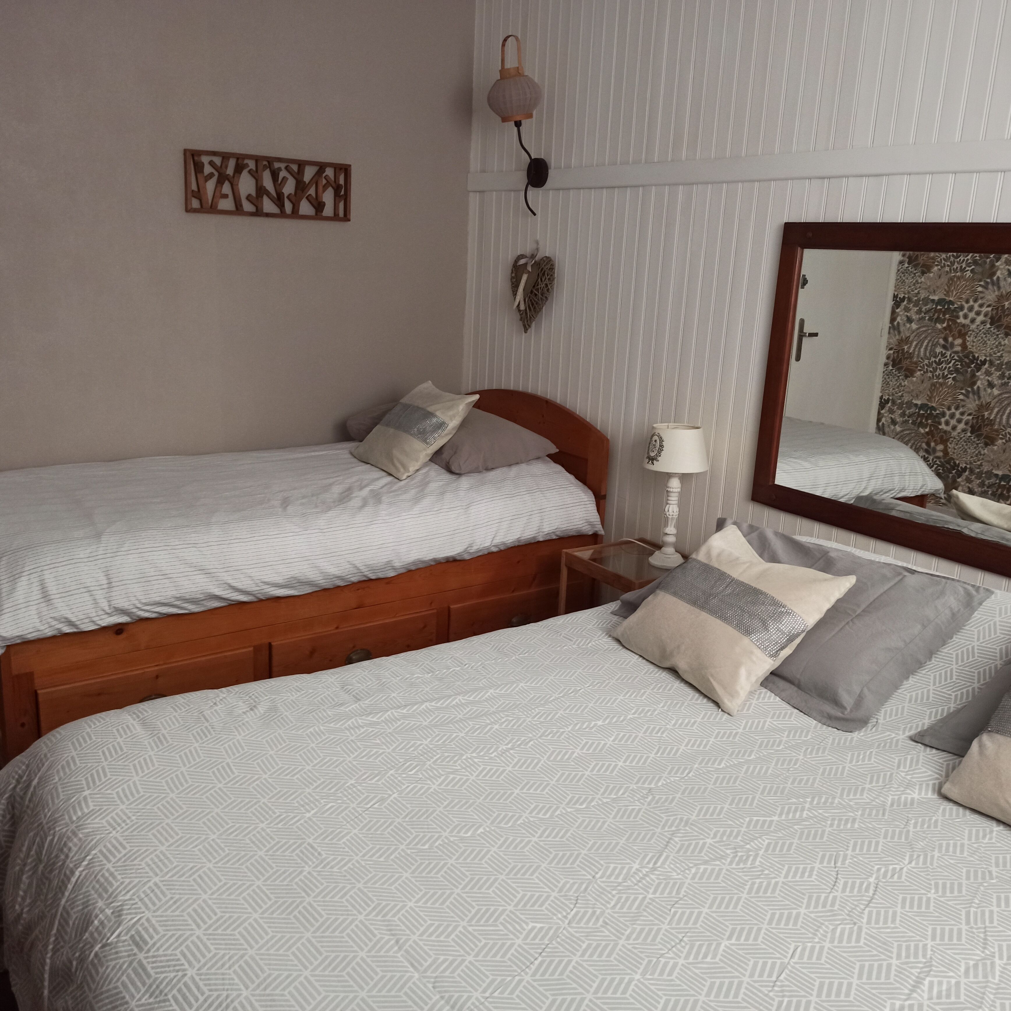 Un dormitorio con dos camas, una mesita de noche con lámpara, un espejo y un adorno en la pared.