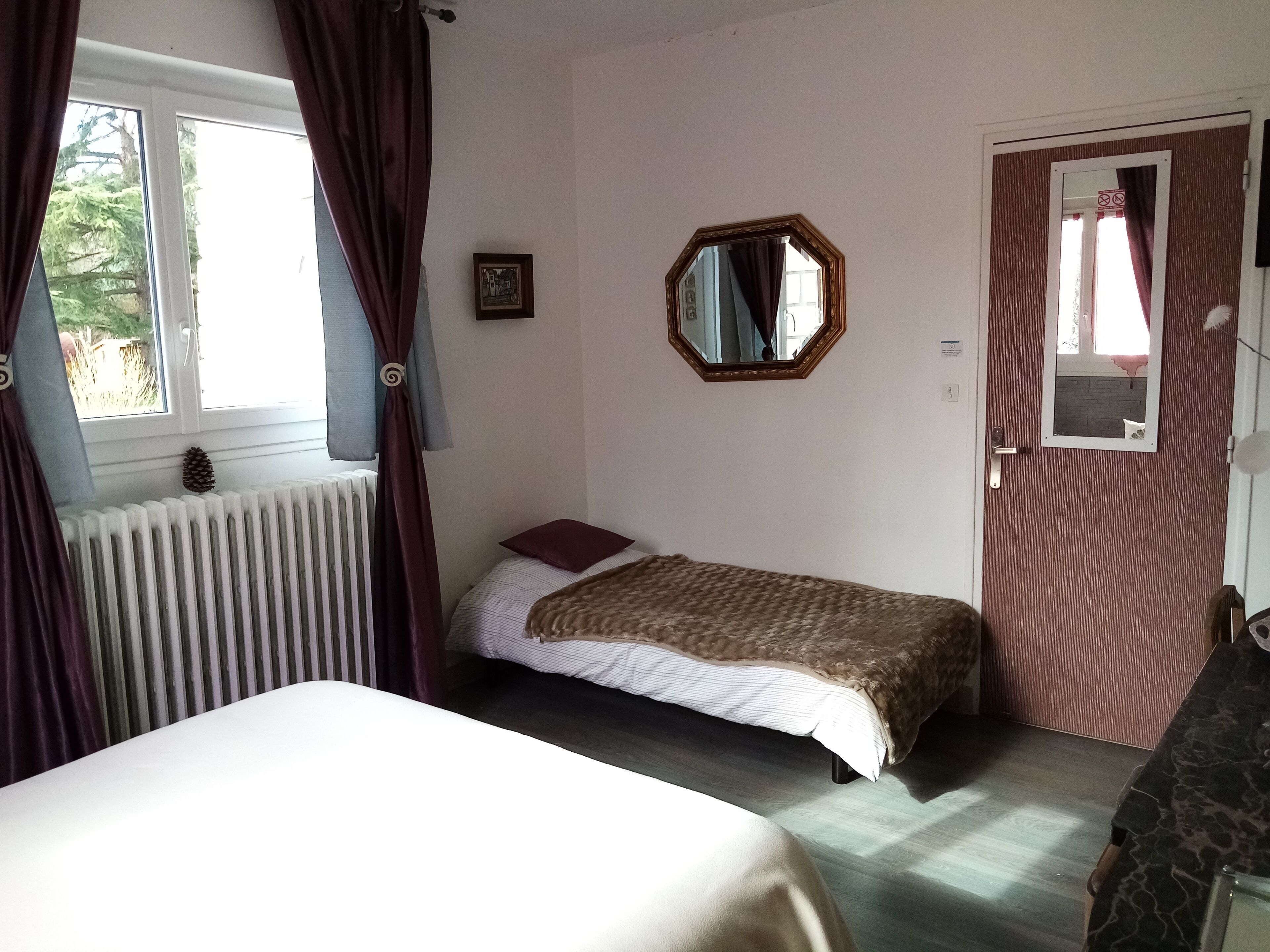 Un dormitorio con una cama individual, un radiador, una ventana con cortinas, una puerta y un espejo en la pared.