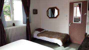 Un dormitorio con una cama individual, un radiador, una ventana con cortinas, una puerta y un espejo en la pared.