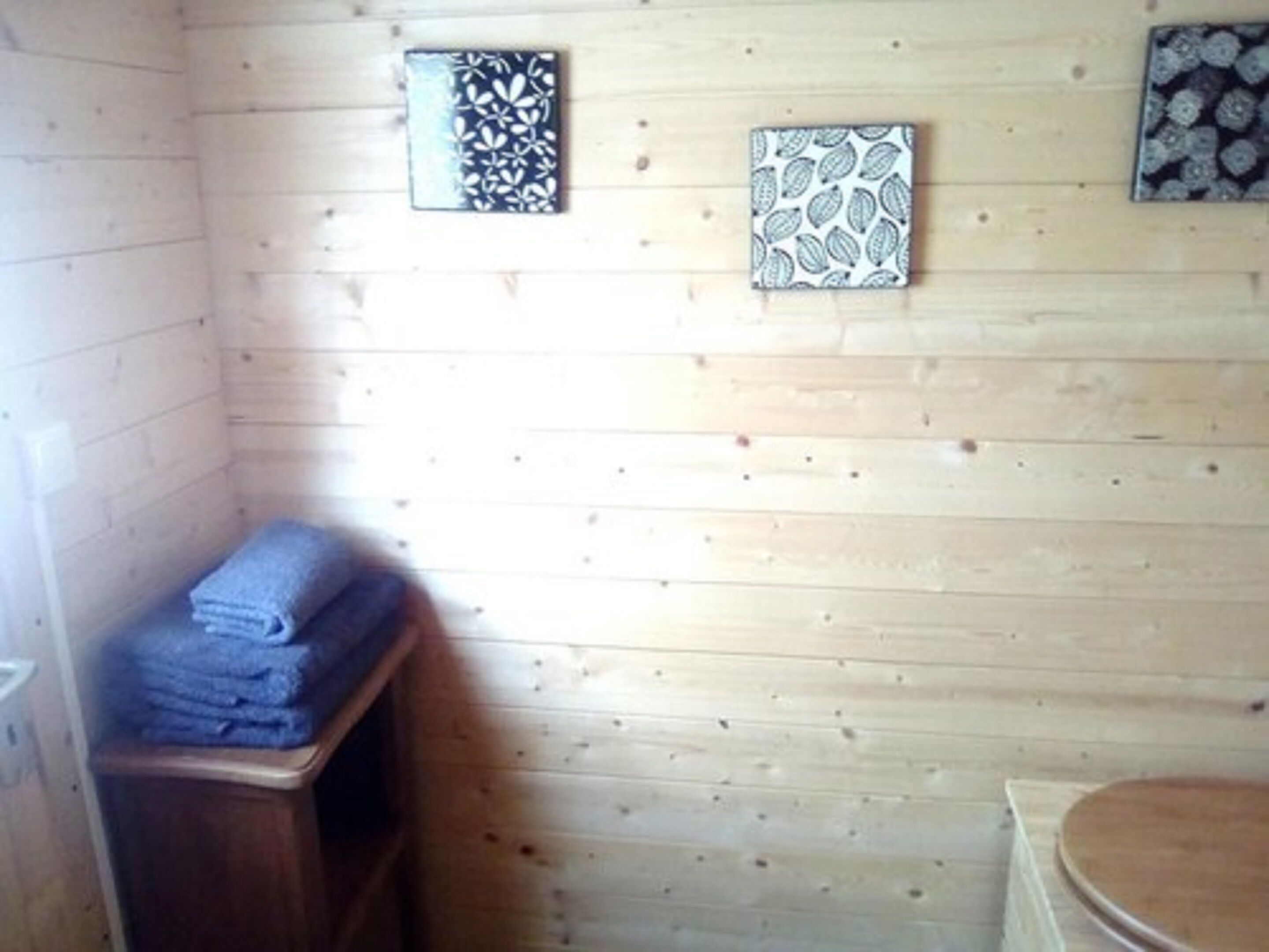 Una habitación con paneles de madera, un banco de madera, una pila de toallas y un inodoro de madera.
