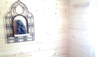 A corner of a room with wooden walls, a small trash bin, and a decorative metal mirror with a sculpture.