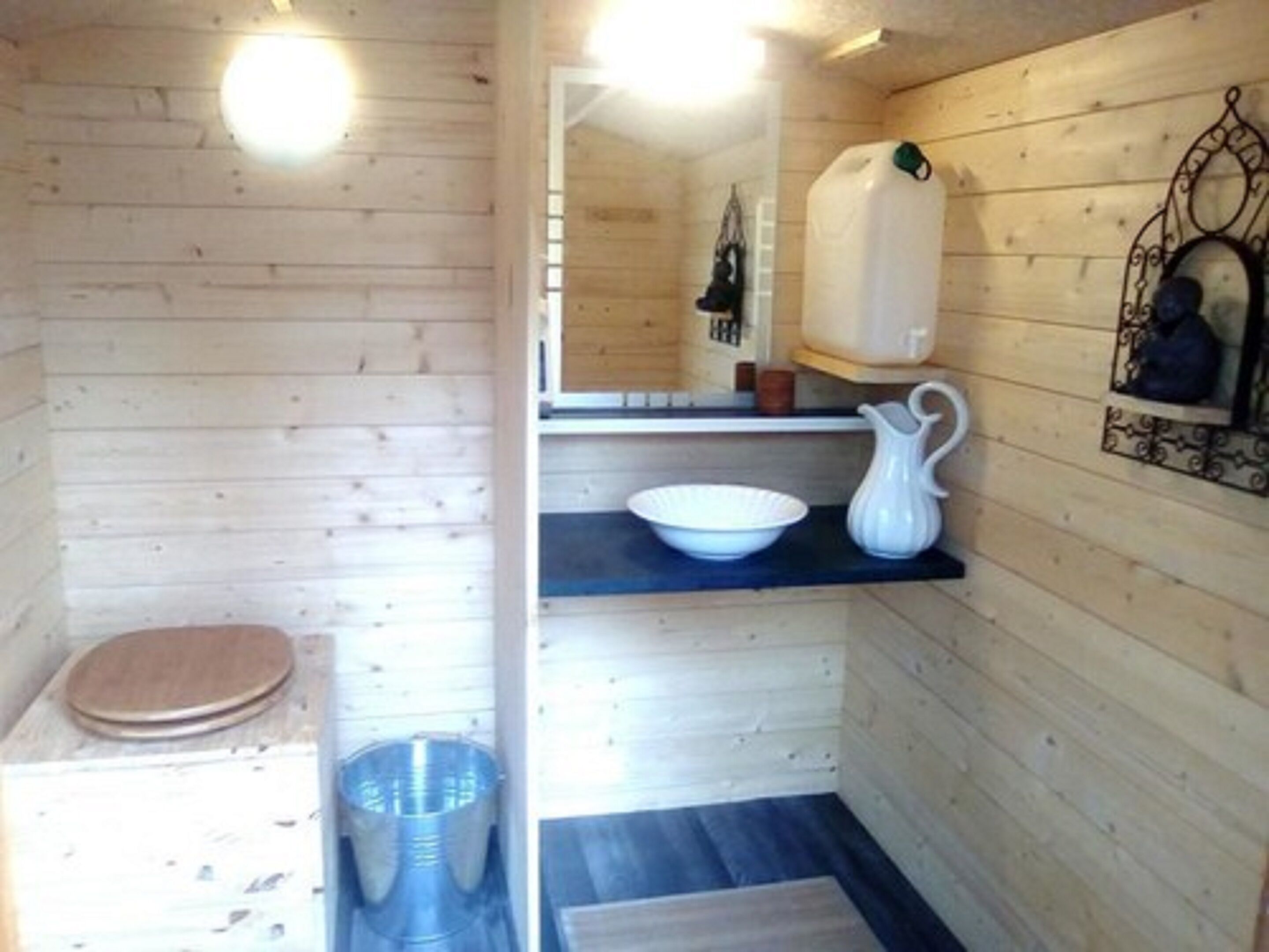 Ein Holzhäuschen im Inneren mit Holzboden, einem weißen Waschbecken, einer weißen Schüssel und einem hölzernen Hocker.