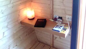 A small, cozy room with wooden walls and a sloped ceiling. There is a shelf with a candle, a book, and a glass. - Les Tonneaux de l'Eure Logement Insolite (Neuilly)