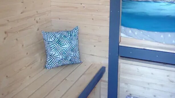 A wooden cabin room with a bed, a heart-shaped wall decoration, and a patterned pillow. - Les Tonneaux de l'Eure Logement Insolite (Neuilly)