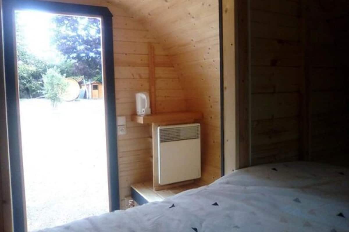 Una cabaña pequeña de una sola habitación con cama, calefacción y ventana.