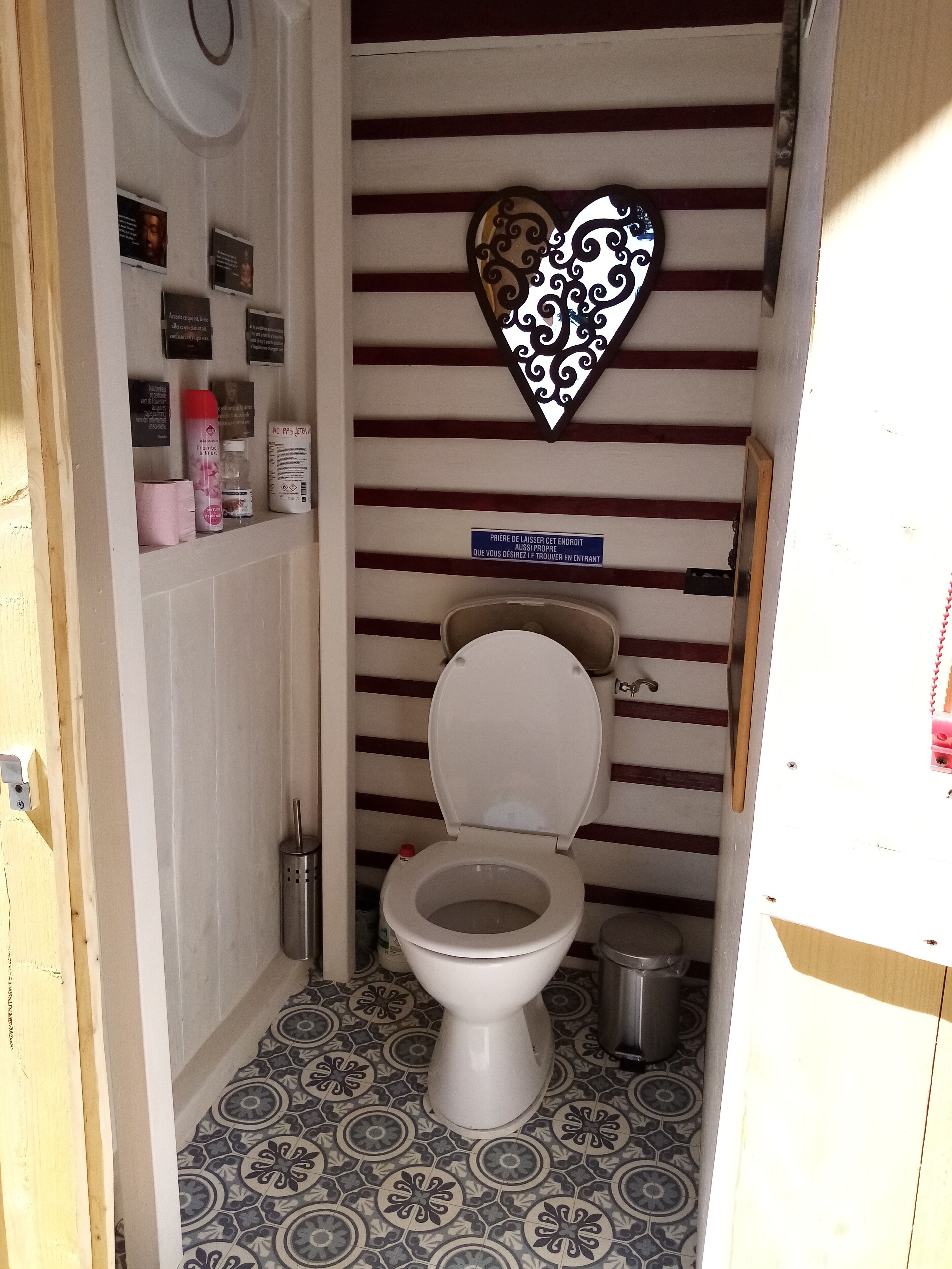 Un baño pequeño y funcional con un adorno en forma de corazón en la pared, un inodoro y una estantería con artículos de aseo.