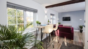 Ein modernes Wohnzimmer mit einem roten Sofa, einem Essbereich mit Tisch und Stühlen und einem an der Wand befestigten Fernseher.