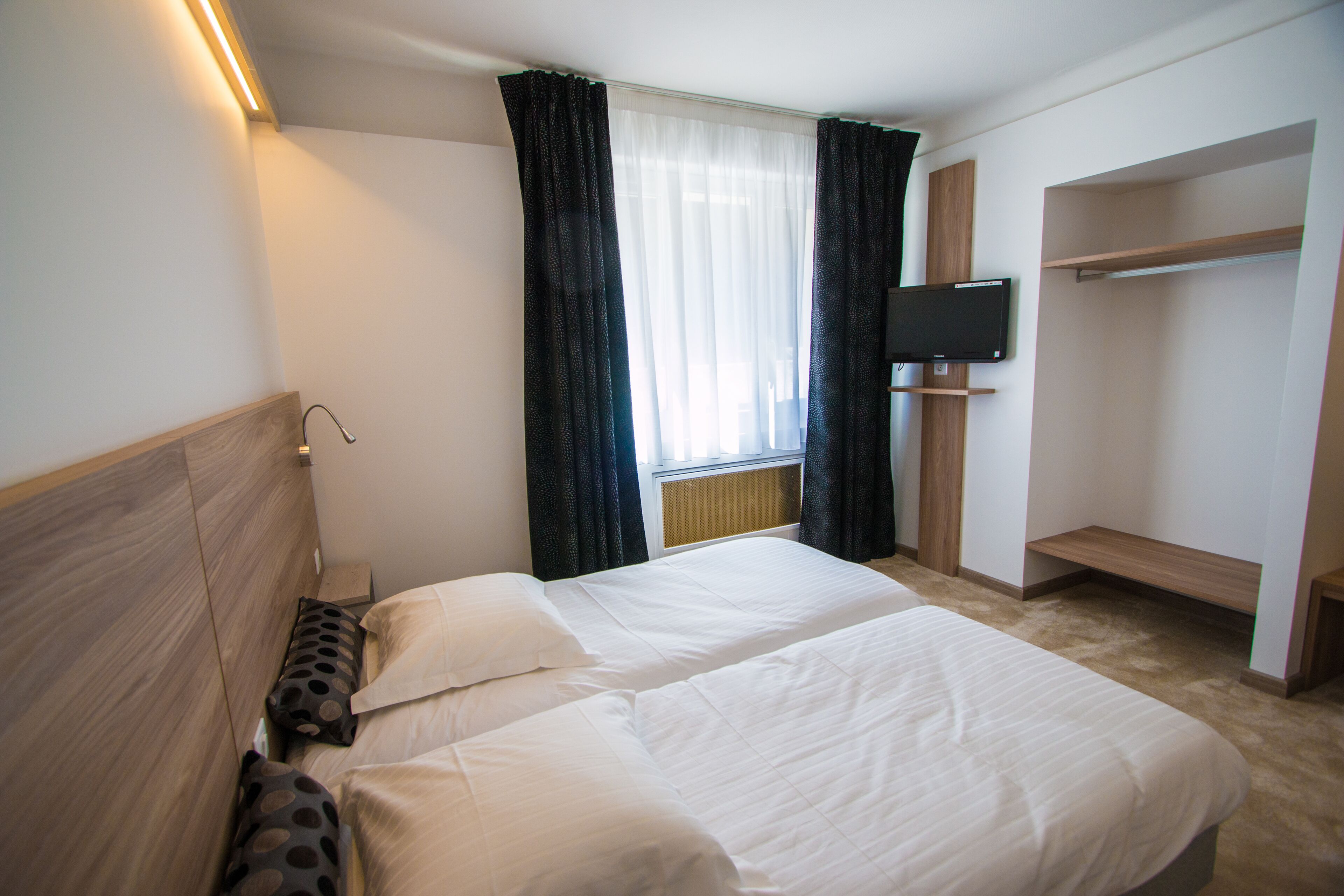 Ein Hotelzimmer mit zwei Betten, einem an der Wand befestigten Fernseher und einem eingebauten Kleiderschrank.