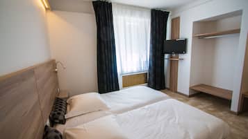 Ein Hotelzimmer mit zwei Betten, einem an der Wand befestigten Fernseher und einem eingebauten Kleiderschrank.
