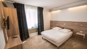 A modern hotel room with a wooden headboard, a bed with white linens, a bedside table, and a built-in TV.
