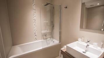 A modern bathroom with a glass-enclosed shower, a white bathtub, and a wooden vanity with a sink.