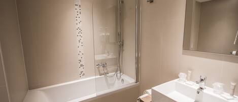 Un baño moderno con ducha envuelta en vidrio, una bañera blanca y un tocador de madera con lavamanos.