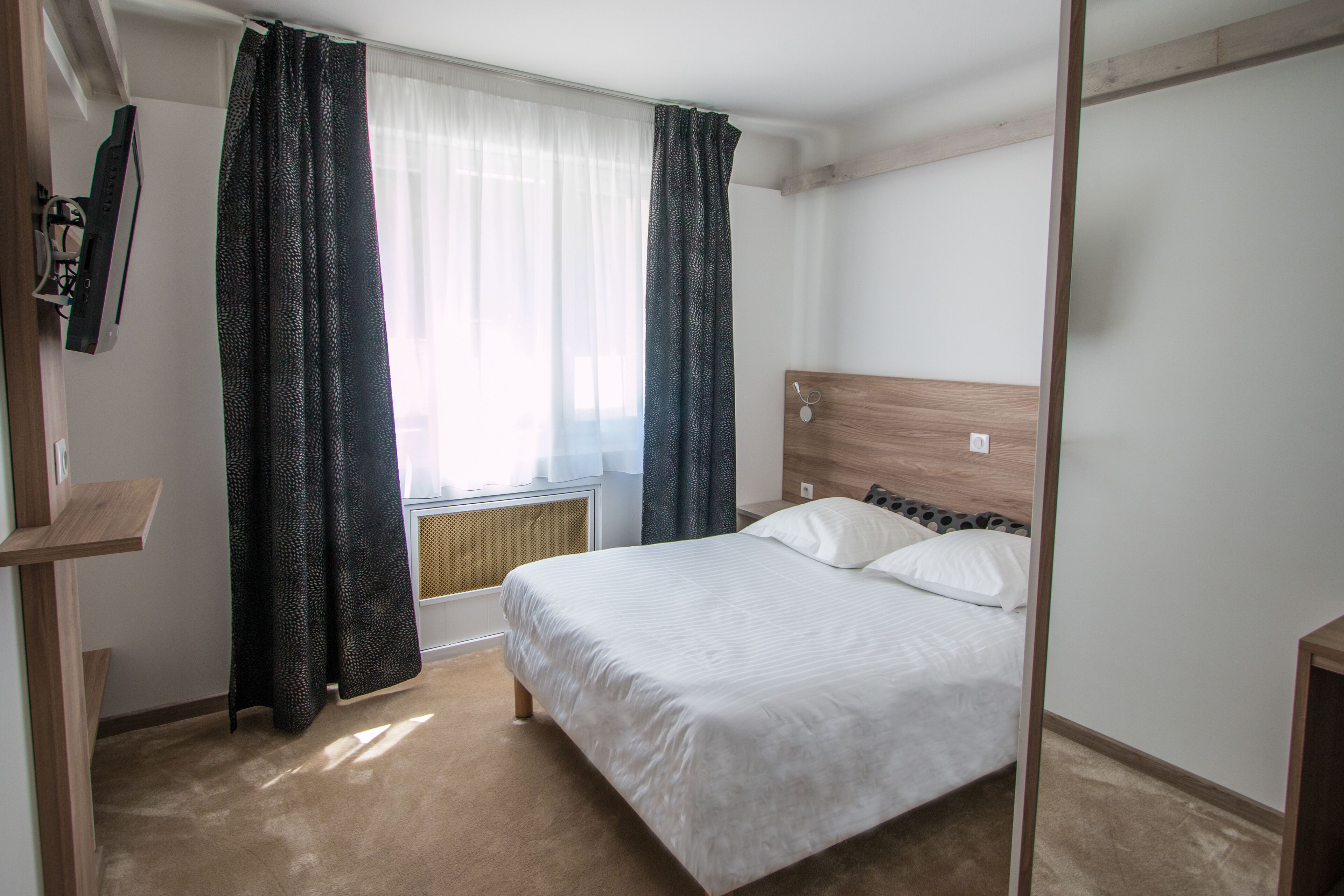 Un dormitorio con cama, ventana con cortinas, radiador y cabecero de madera.