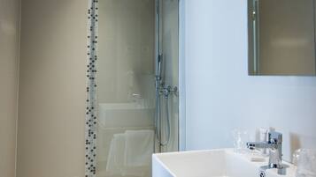 Un baño moderno con ducha de vidrio, un lavamanos espacioso y un espejo.
