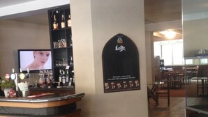 Zona de bar con taburetes, una pantalla de televisión y estantes con botellas.