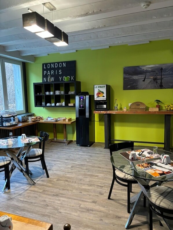Una cafetería moderna con una pared verde, una máquina de café y un cartel que menciona Londres, París y Nueva York.