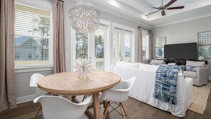 Un salon moderne avec une table ronde en bois, des chaises blanches, un canapé blanc et un téléviseur.