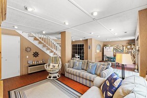 A spacious living room with a striped sofa, a striped armchair, and a staircase leading to another level.