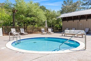 A swimming pool with a surrounding deck, lounge chairs, and a covered seating area.