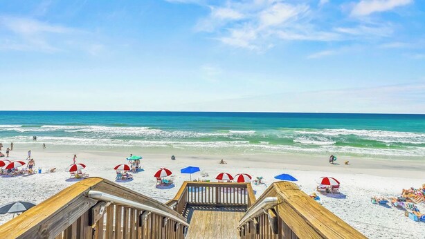 Een houten looppad naar een strand met parasols en strandstoelen.