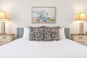 Un lit bien fait, recouvert d’une couette blanche, avec deux lampes de chevet et une œuvre d’art florale encadrée au-dessus du lit.
